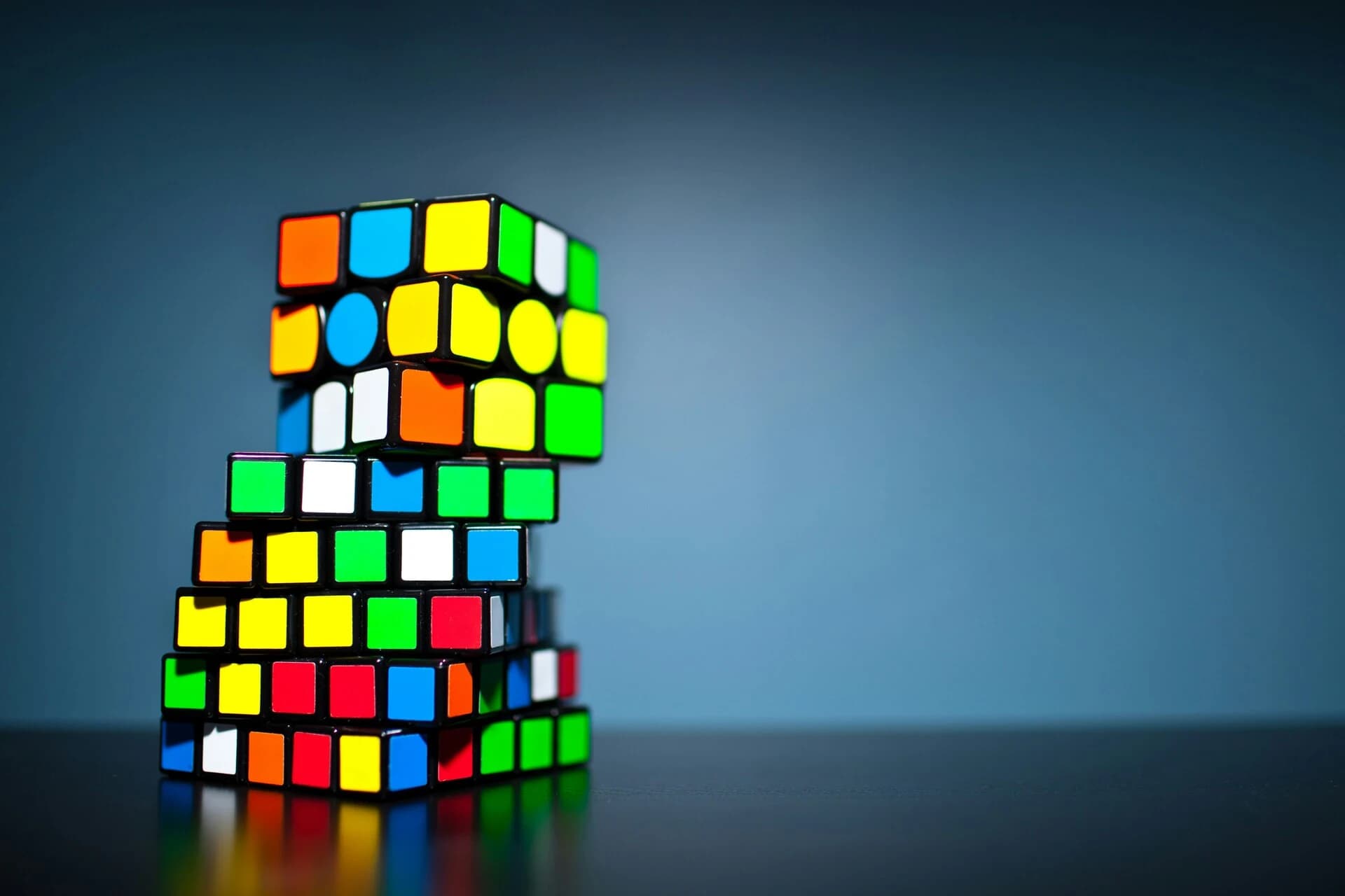 A stack of Rubik's cubes on a black table with a blue background